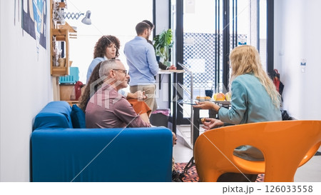 Colleagues relaxing in a modern office break area, chatting over snacks. 126033558
