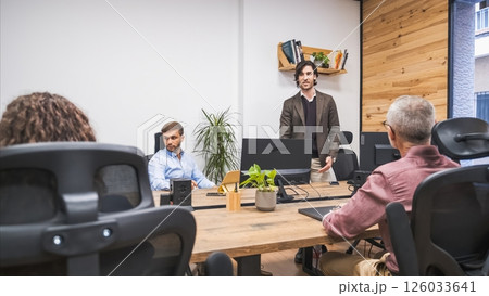 Confident businessman talking to team sitting at computer desks in creative office Confident businessman talking to team sitting at computer desks in creative office 126033641