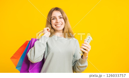 Smiling woman holding shopping bags and using smartphone on yellow background Smiling woman holding shopping bags and using smartphone on yellow background 126033757
