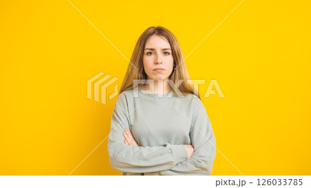 Serious young woman crossing arms on yellow background Serious young woman crossing arms on yellow background 126033785