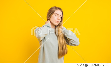 Young woman massaging neck suffering from pain on yellow background 126033792