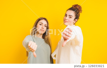 Two young women showing thumbs down on yellow background 126033821
