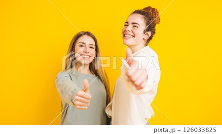 Two happy women showing thumbs up on yellow background 126033825