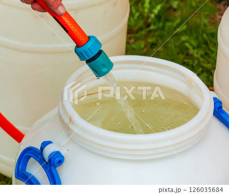 A woman's hand fills a plastic barrel with water from a hose. The concept of the drinking water crisis in the world. 126035684
