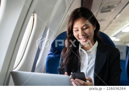 Business travel woman smiling using phone and laptop in airplane Business travel woman smiling using phone and laptop in airplane 126036264