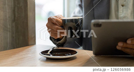 Elderly man holding a coffee cup and using a tablet in a cafe, reflecting on business matters. Elderly man holding a coffee cup and using a tablet in a cafe, reflecting on business matters. 126036986