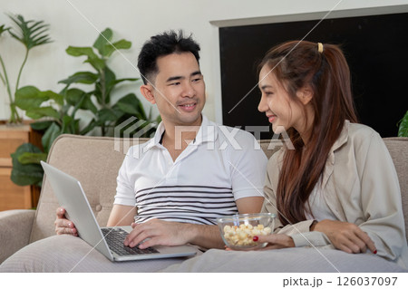 Couple enjoying a movie together on a laptop with popcorn. 126037097