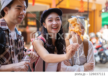 Friends exploring local street food, enjoying laughter while tasting delicious snacks during travel 126037111