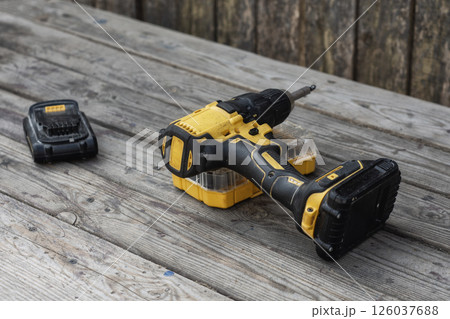 Yellow Cordless electric drill and battery charger on wooden background for DIY projects and repairs. 126037688