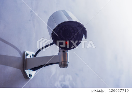CCTV security camera with a glowing red light is mounted on a gray wall. Security and technology concept. 126037719