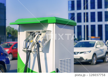 Electronic charging for an electric car. Electric vehicle charging station in the city with cars in the background. Electronic charging for an electric car. Electric vehicle charging station in the city with cars in the background. 126037758