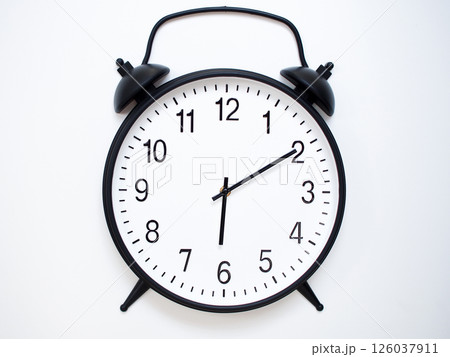 Black Retro Alarm Clock Showing 06:10 or 18:10. Classic Bell Style on White Wood Background. 126037911