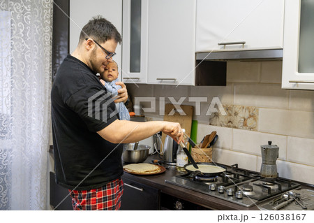 Father Cooking Pancakes While Holding Baby Father Cooking Pancakes While Holding Baby 126038167