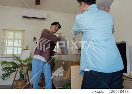 Gay couple playfully throwing pillows during unpacking in their new home. 126038488