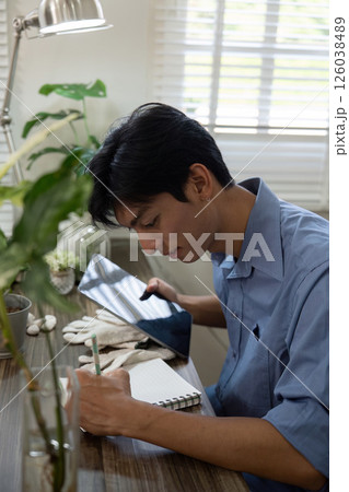 Gardening and Creativity. A young man focuses on his planting process by writing notes. 126038489
