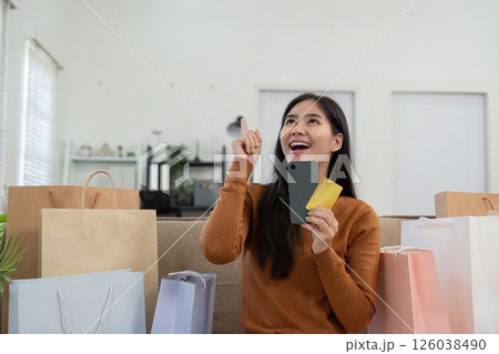 Joyful woman celebrating her online shopping success at home, holding credit cards and smiling. 126038490