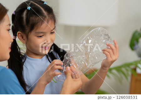 Educational Recycling Activity. A child excitedly learns about recycling plastic bottles with her mother in a home setting. 126038531
