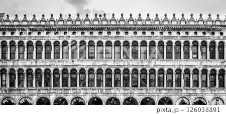 The Old Procuracies at Saint Marc Square showcase intricate architectural details, highlighting Venetian design and craftsmanship from a bygone era, framed against a moody sky. 126038891