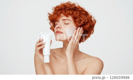 Red-haired woman gently applying dermatological cream to sensitive fair skin, highlighting innovative skincare solutions for irritation, allergy, and redness treatment. 126039986