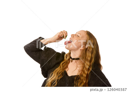 Woman in black dress tilts head back, squeezing green lime into open mouth against white studio background. Woman in black dress tilts head back, squeezing green lime into open mouth against white studio background. 126040387