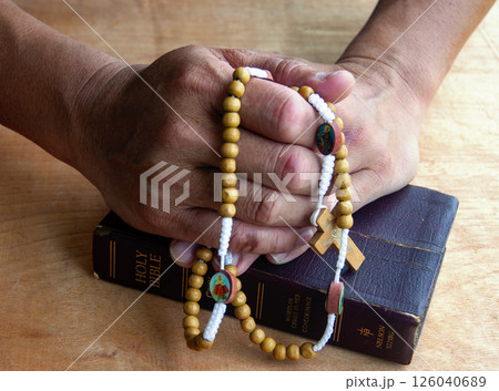 Hands clutching Holy Rosary beads tell the story of heartfelt prayers whispered in moments of need and hope. 126040689