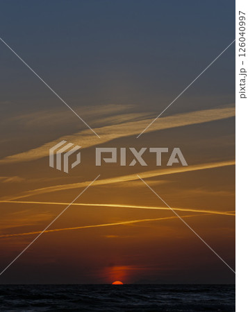 夕焼け空に描かれた飛行機雲と沈む太陽 126040997