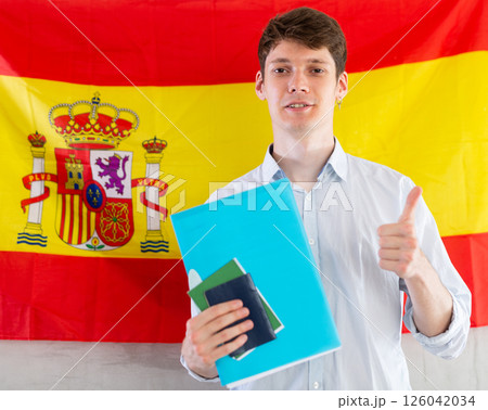 Young guy posing with documents on background of flag of Spain Young guy posing with documents on background of flag of Spain 126042034
