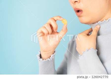 Woman taking medical lozenges with honey lemon flavored for relief sore throat, irritating cough and mouth pain. Close up of female feeling sick and cold over light blue backgroud. Health care. Woman taking medical lozenges with honey lemon flavored for relief sore throat, irritating cough and mouth pain. Close up of female feeling sick and cold over light blue backgroud. Health care. 126042770
