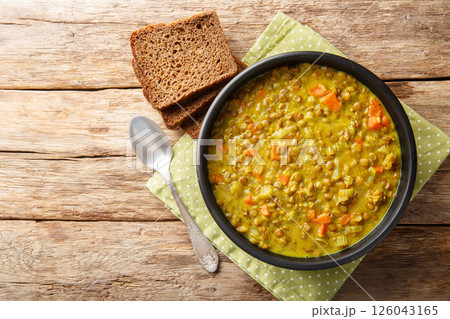 Thick healthy green lentil soup with coconut milk, carrot, onion, turmeric, lemon and ginger close-up in a plate. Horizontal top view 126043165