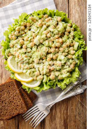 Diet protein salad with chickpeas, mashed avocado, onion and celery served with whole grain bread close-up in a plate on the table. Vertical top view 126043184