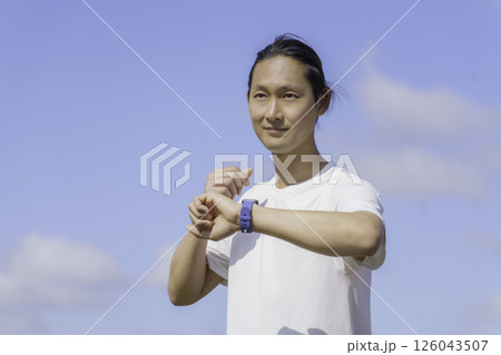 多摩川の土手をランニングしながらスマートウォッチをチェックする若い男性 126043507