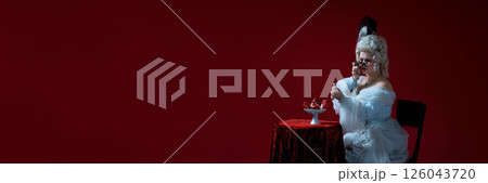 Dramatic scene. Woman in historical image raising opera glasses above red table and expecting pomegranates against deep red background Dramatic scene. Woman in historical image raising opera glasses above red table and expecting pomegranates against deep red background 126043720