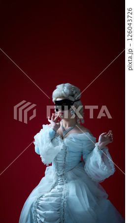 Silent gesture. Noblewoman in corseted dress striking expressive pose with mask on, embracing theatrical flair. 126043726