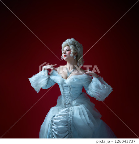 Vintage portrait of young graceful woman in image of medieval royal person in renaissance style dress on deep red background. 126043737