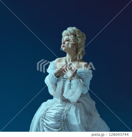 Dramatic silence. Noblewoman in powdered wig and vintage blue gown holding hands to chest. 126043744