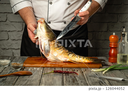 A skilled chef expertly fillets a freshly caught fish on a wooden cutting board. Various ingredients and kitchen tools are arranged nearby, enhancing the culinary atmosphere A skilled chef expertly fillets a freshly caught fish on a wooden cutting board. Various ingredients and kitchen tools are arranged nearby, enhancing the culinary atmosphere 126044052