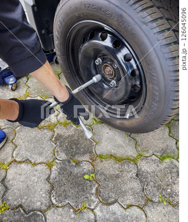 Nitra, Slovakia - 08.05.2025: Car service. Wheel replacement. Seasonal tire change. The mechanic removes the wheel with both hands and key. 126045096