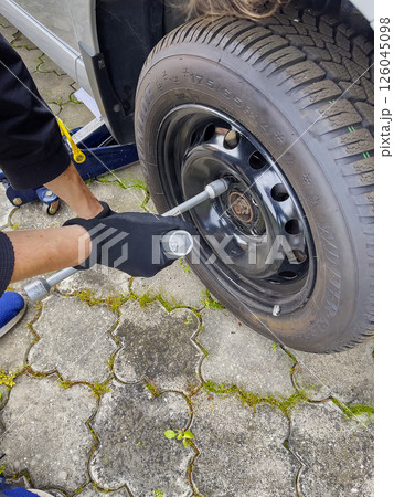 Nitra, Slovakia - 08.05.2025: Car service. Wheel replacement. Seasonal tire change. The mechanic removes wheel with both hands and key. 126045098
