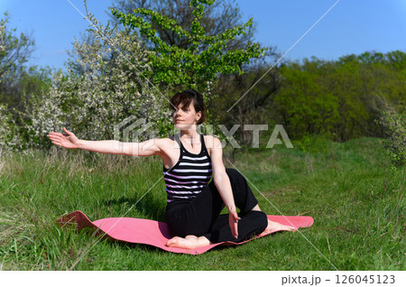 Woman practicing seated spinal twist pose outdoors in spring garden. 126045123