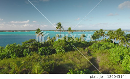 Stunning aerial view of a tropical island lush greenery, turquoise water, boats in lagoon. Palm trees sway gently in breeze, creating a serene paradise atmosphere. Exotic travel getaway. Drone flight Stunning aerial view of a tropical island lush greenery, turquoise water, boats in lagoon. Palm trees sway gently in breeze, creating a serene paradise atmosphere. Exotic travel getaway. Drone flight 126045144