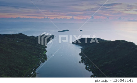 Tranquil aerial view captures a serene coastal landscape. The scene features lush green hills and a calm bay, set against a vibrant sunset sky with scattered clouds. Drone fly over sea ocean water Tranquil aerial view captures a serene coastal landscape. The scene features lush green hills and a calm bay, set against a vibrant sunset sky with scattered clouds. Drone fly over sea ocean water 126045145