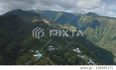 Tahiti island volcanic mountain landscape. Beautiful hills covered rainforest, lush green valleys, scattered houses village buildings under cloudy sky, showcasing French Polynesia beauty. Aerial shot 126045171