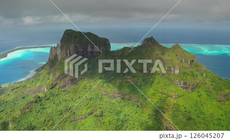 Aerial perspective showcases an island's vibrant green mountains surrounded by stunning turquoise lagoons, revealing a serene coastal community and intricate landscapes Aerial perspective showcases an island's vibrant green mountains surrounded by stunning turquoise lagoons, revealing a serene coastal community and intricate landscapes 126045207