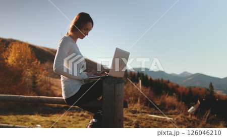 Woman typing on laptop and enjoying autumn sunset mountains nature. Work outdoor, online digital nomad remote job in Carpathian mountains. Outdoor lifestyle travel on summer holiday vacation. 126046210