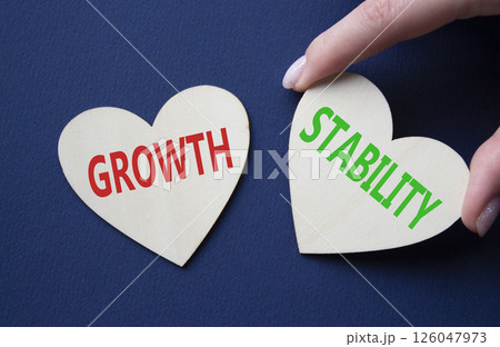 Growth and Stability symbol. Concept word Growth and Stability on wooden hearts. Businessman hand. Beautiful deep blue background. Business and Growth and Stability concept. Copy space 126047973