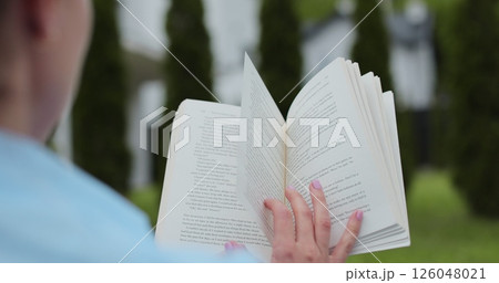 Close-up of a woman hand turning to a new page in the backyard of a house. 126048021