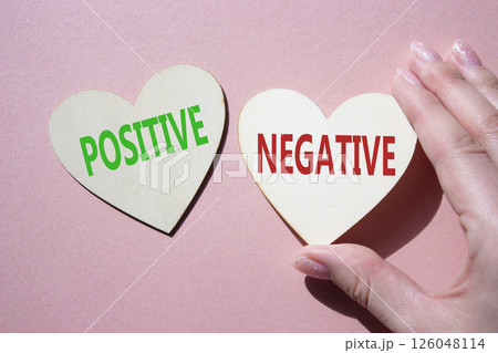 Positive or Negative symbol. Concept word Positive or Negative on wooden hearts. Businessman hand. Beautiful pink background. Business and Positive or Negative concept. Copy space 126048114