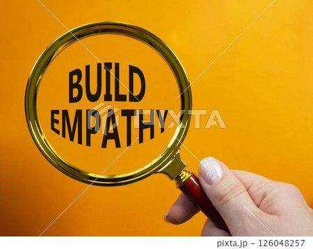 Build empathy symbol. Magnifying glass with words Build empathy. Beautiful orange background. Businessman hand. Business and Build empathy concept. Copy space. 126048257
