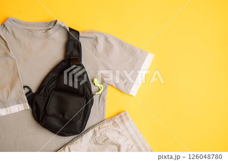 Stylish dark and light grey children's T-shirt with jeans and black bag. Fashion kids outfit for summer, autumn. Total grey look on yellow background. Flat lay, top view 126048780