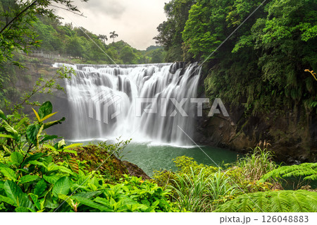 Shifen Waterfall in Pingxi District of New Taipei, Taiwan, cascades powerfully into a turquoise pool amid dense green foliage, offering a scenic and tranquil natural attraction often called the Little 126048883